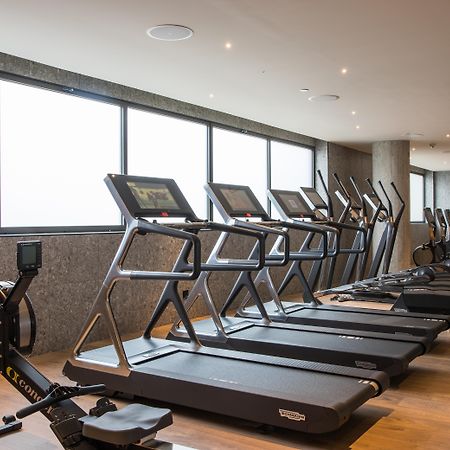 Hotel Grand Hyatt Barcelona Exteriér fotografie The photo shows a modern gym space featuring several pieces of exercise equipment. In the foreground, there are treadmills, while in the background, there are elliptical machines lined up against large windows that provide natural light. The flooring