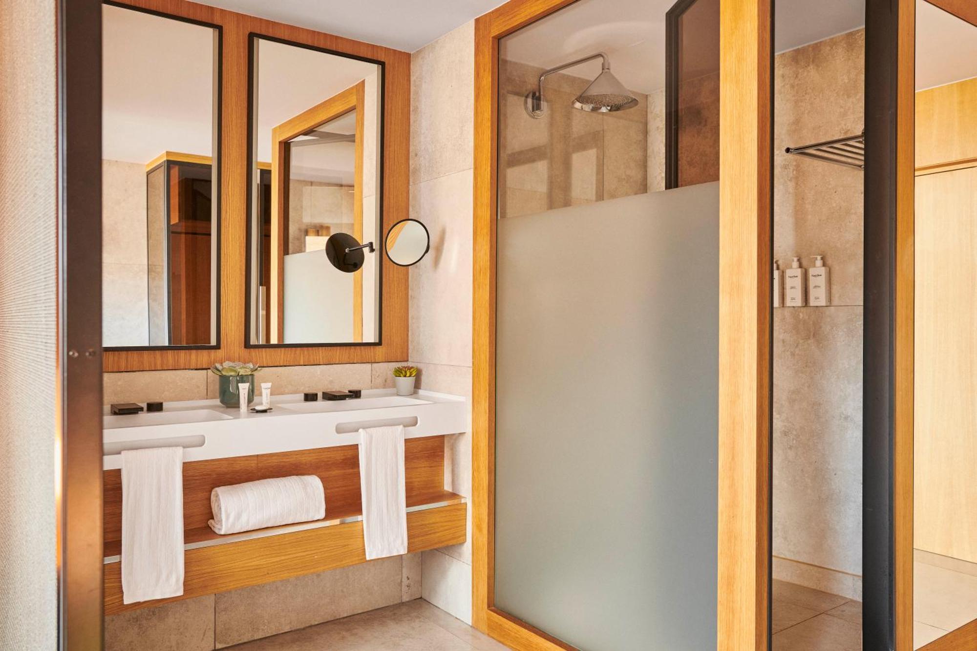 Hotel Grand Hyatt Barcelona Exteriér fotografie The photo depicts a modern bathroom featuring a combination of natural materials and sleek design. There are three mirrors mounted on the wall above a wooden vanity. The vanity includes a basin and is adorned with toiletries and a small plant. On the